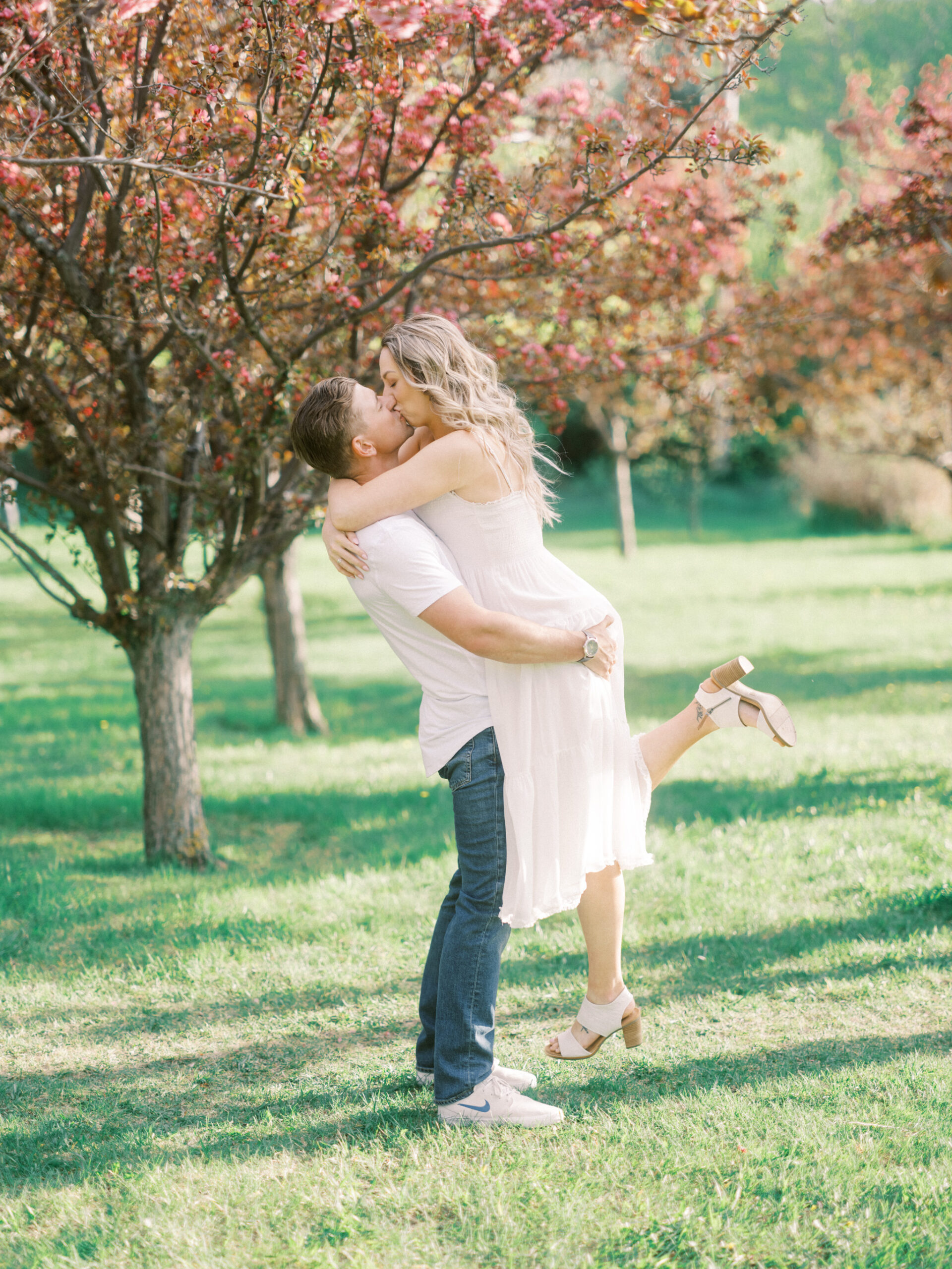 Cherry Blossom Spring Engagement Session, river engagement couple laughing, couple embracing, engagement pose sunset, sunset engagement photos, labrador retriever engagement photos, dog engagement session, puppy engagement session, alberta wedding photographers, alberta photographer, calgary wedding, calgary wedding photographer, spring engagement session, spring photos, nicole sarah, cherry blossom photos, cherry blossom engagement, wedding poses, white dress engagement, sundress white, engagement photos, bow river, puppy engagement photos, neutral engagement photos