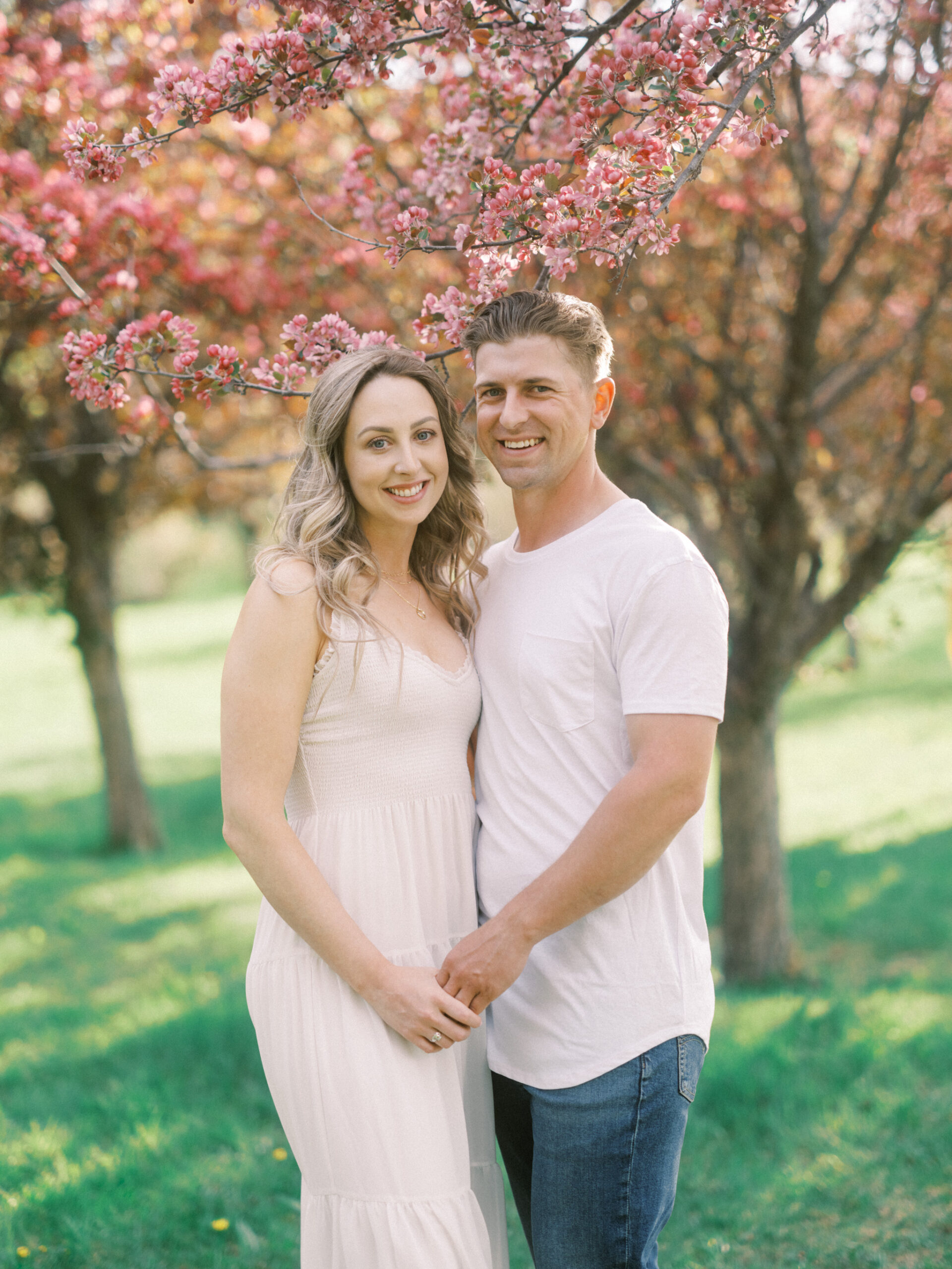 Cherry Blossom Spring Engagement Session, river engagement couple laughing, couple embracing, engagement pose sunset, sunset engagement photos, labrador retriever engagement photos, dog engagement session, puppy engagement session, alberta wedding photographers, alberta photographer, calgary wedding, calgary wedding photographer, spring engagement session, spring photos, nicole sarah, cherry blossom photos, cherry blossom engagement, wedding poses, white dress engagement, sundress white, engagement photos, bow river, puppy engagement photos, neutral engagement photos