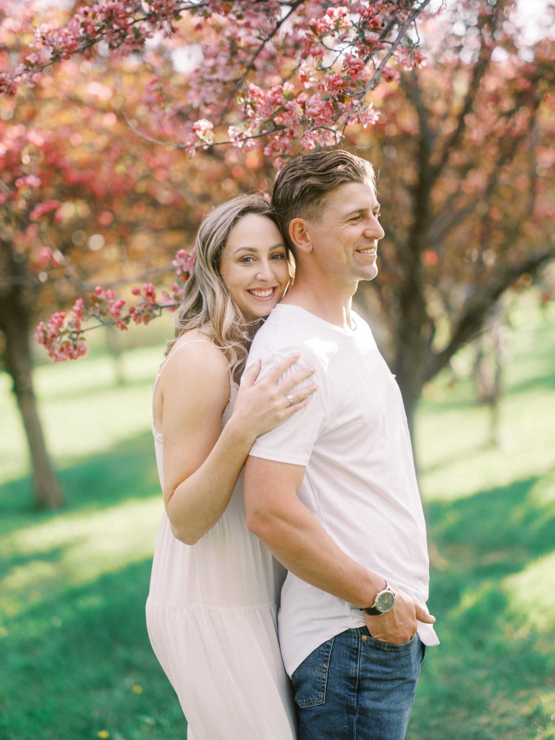 Cherry Blossom Spring Engagement Session, river engagement couple laughing, couple embracing, engagement pose sunset, sunset engagement photos, labrador retriever engagement photos, dog engagement session, puppy engagement session, alberta wedding photographers, alberta photographer, calgary wedding, calgary wedding photographer, spring engagement session, spring photos, nicole sarah, cherry blossom photos, cherry blossom engagement, wedding poses, white dress engagement, sundress white, engagement photos, bow river, puppy engagement photos, neutral engagement photos