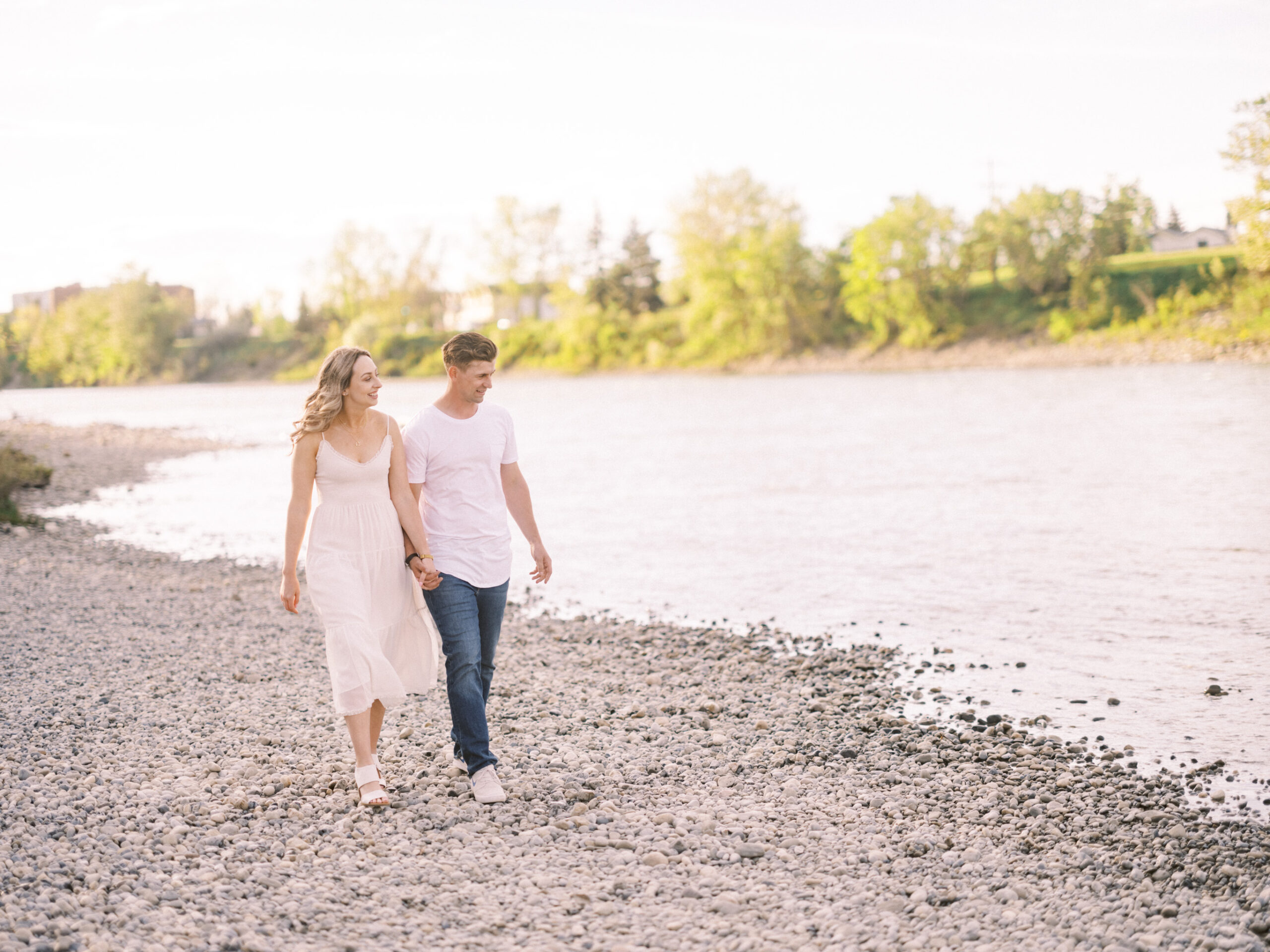 Cherry Blossom Spring Engagement Session, river engagement couple laughing, couple embracing, engagement pose sunset, sunset engagement photos, labrador retriever engagement photos, dog engagement session, puppy engagement session, alberta wedding photographers, alberta photographer, calgary wedding, calgary wedding photographer, spring engagement session, spring photos, nicole sarah, cherry blossom photos, cherry blossom engagement, wedding poses, white dress engagement, sundress white, engagement photos, bow river, puppy engagement photos, neutral engagement photos