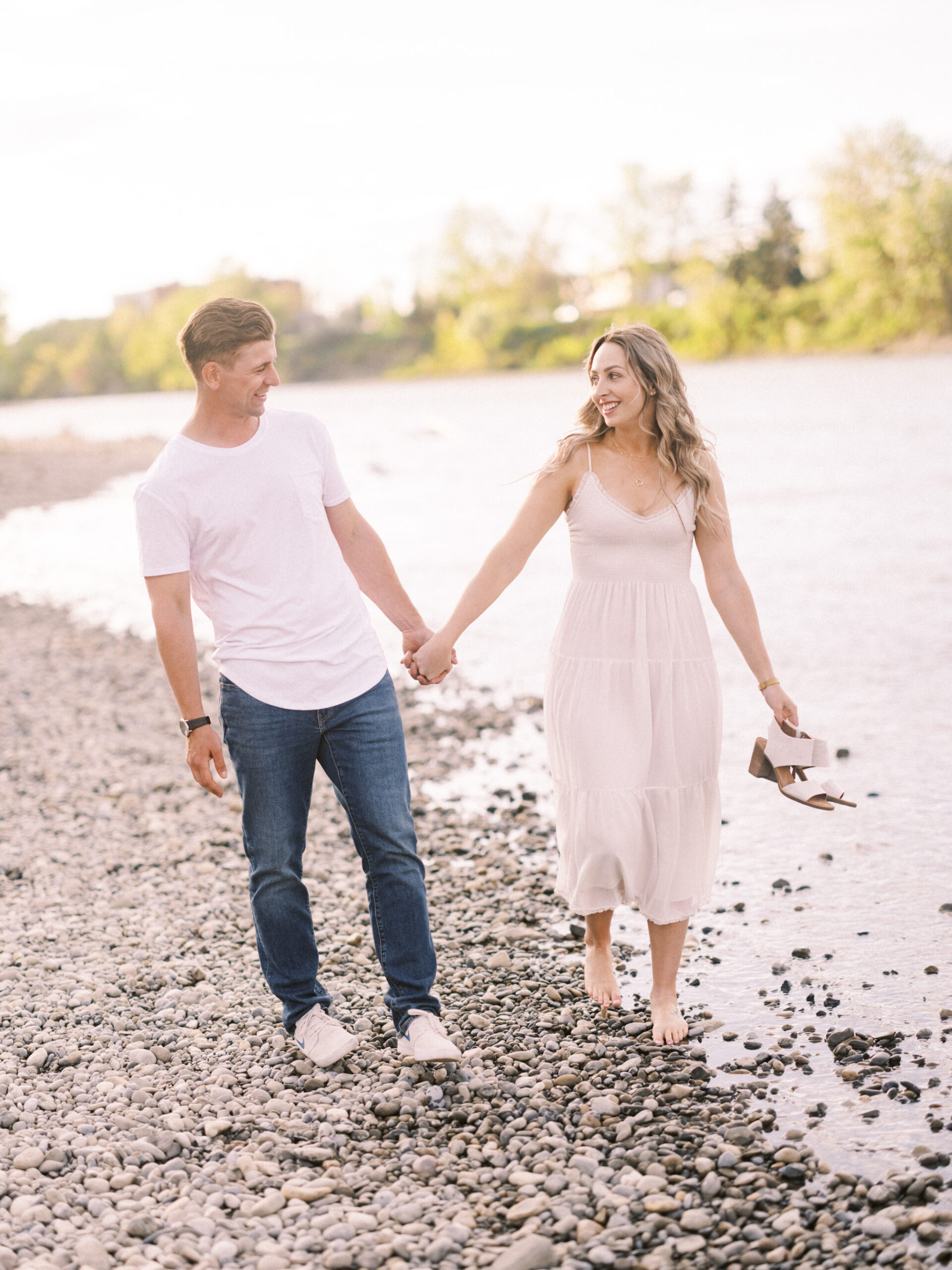 Cherry Blossom Spring Engagement Session, river engagement couple laughing, couple embracing, engagement pose sunset, sunset engagement photos, labrador retriever engagement photos, dog engagement session, puppy engagement session, alberta wedding photographers, alberta photographer, calgary wedding, calgary wedding photographer, spring engagement session, spring photos, nicole sarah, cherry blossom photos, cherry blossom engagement, wedding poses, white dress engagement, sundress white, engagement photos, bow river, puppy engagement photos, neutral engagement photos