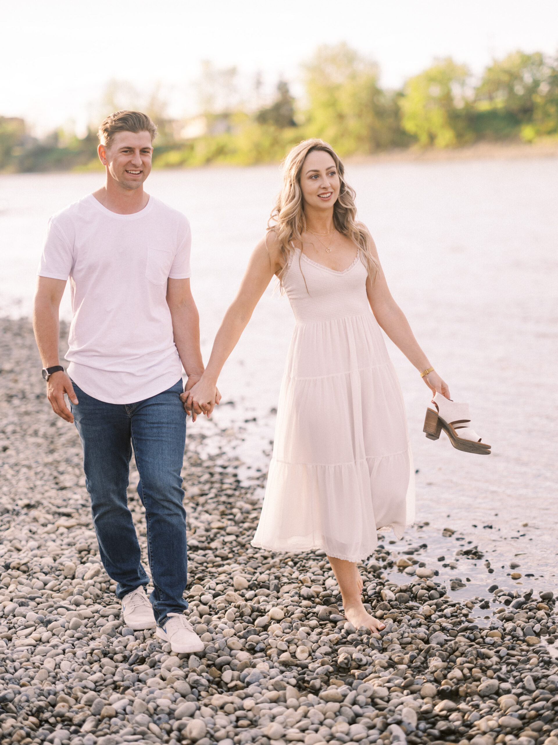 Cherry Blossom Spring Engagement Session, river engagement couple laughing, couple embracing, engagement pose sunset, sunset engagement photos, labrador retriever engagement photos, dog engagement session, puppy engagement session, alberta wedding photographers, alberta photographer, calgary wedding, calgary wedding photographer, spring engagement session, spring photos, nicole sarah, cherry blossom photos, cherry blossom engagement, wedding poses, white dress engagement, sundress white, engagement photos, bow river, puppy engagement photos, neutral engagement photos