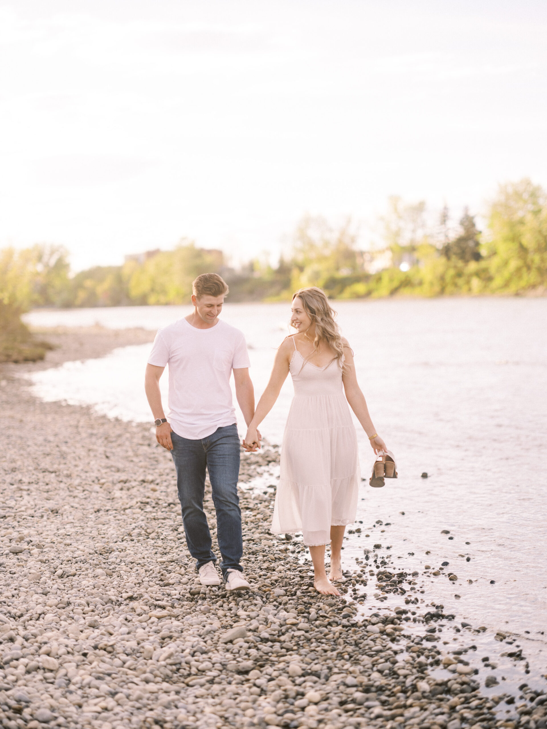 Cherry Blossom Spring Engagement Session, river engagement couple laughing, couple embracing, engagement pose sunset, sunset engagement photos, labrador retriever engagement photos, dog engagement session, puppy engagement session, alberta wedding photographers, alberta photographer, calgary wedding, calgary wedding photographer, spring engagement session, spring photos, nicole sarah, cherry blossom photos, cherry blossom engagement, wedding poses, white dress engagement, sundress white, engagement photos, bow river, puppy engagement photos, neutral engagement photos