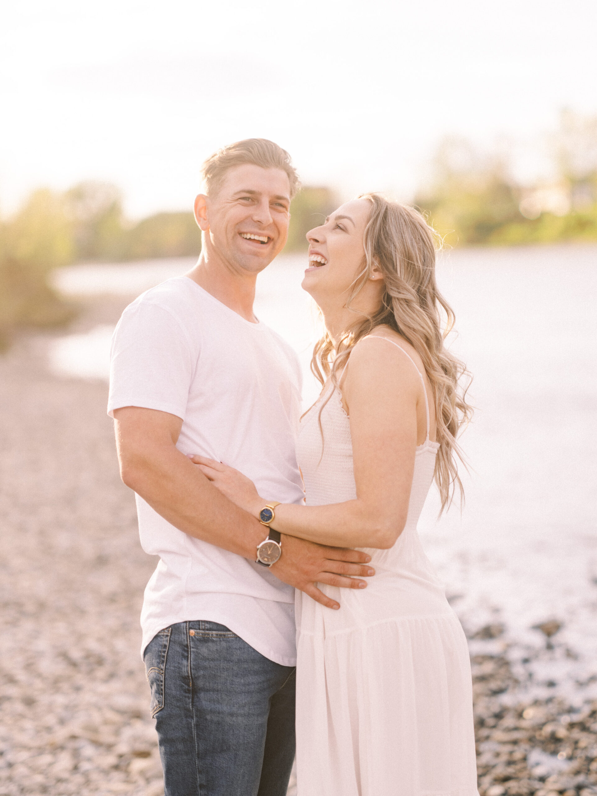 Cherry Blossom Spring Engagement Session, river engagement couple laughing, couple embracing, engagement pose sunset, sunset engagement photos, labrador retriever engagement photos, dog engagement session, puppy engagement session, alberta wedding photographers, alberta photographer, calgary wedding, calgary wedding photographer, spring engagement session, spring photos, nicole sarah, cherry blossom photos, cherry blossom engagement, wedding poses, white dress engagement, sundress white, engagement photos, bow river, puppy engagement photos, neutral engagement photos