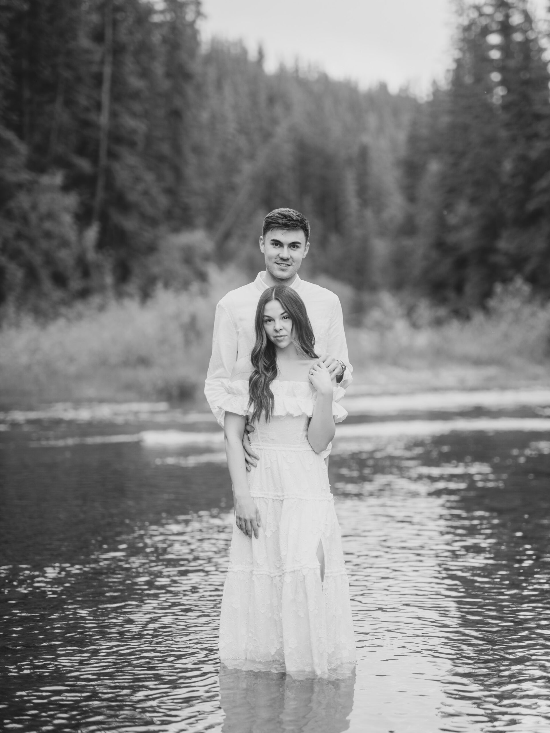 Riverside calgary engagement, forest engagement, bride in white ruffled dress engagement, groom and bride sitting by the river, bride and groom standing in river, standing in sunset forest, nicole sarah, calgary wedding photographers, fish creek park engagement