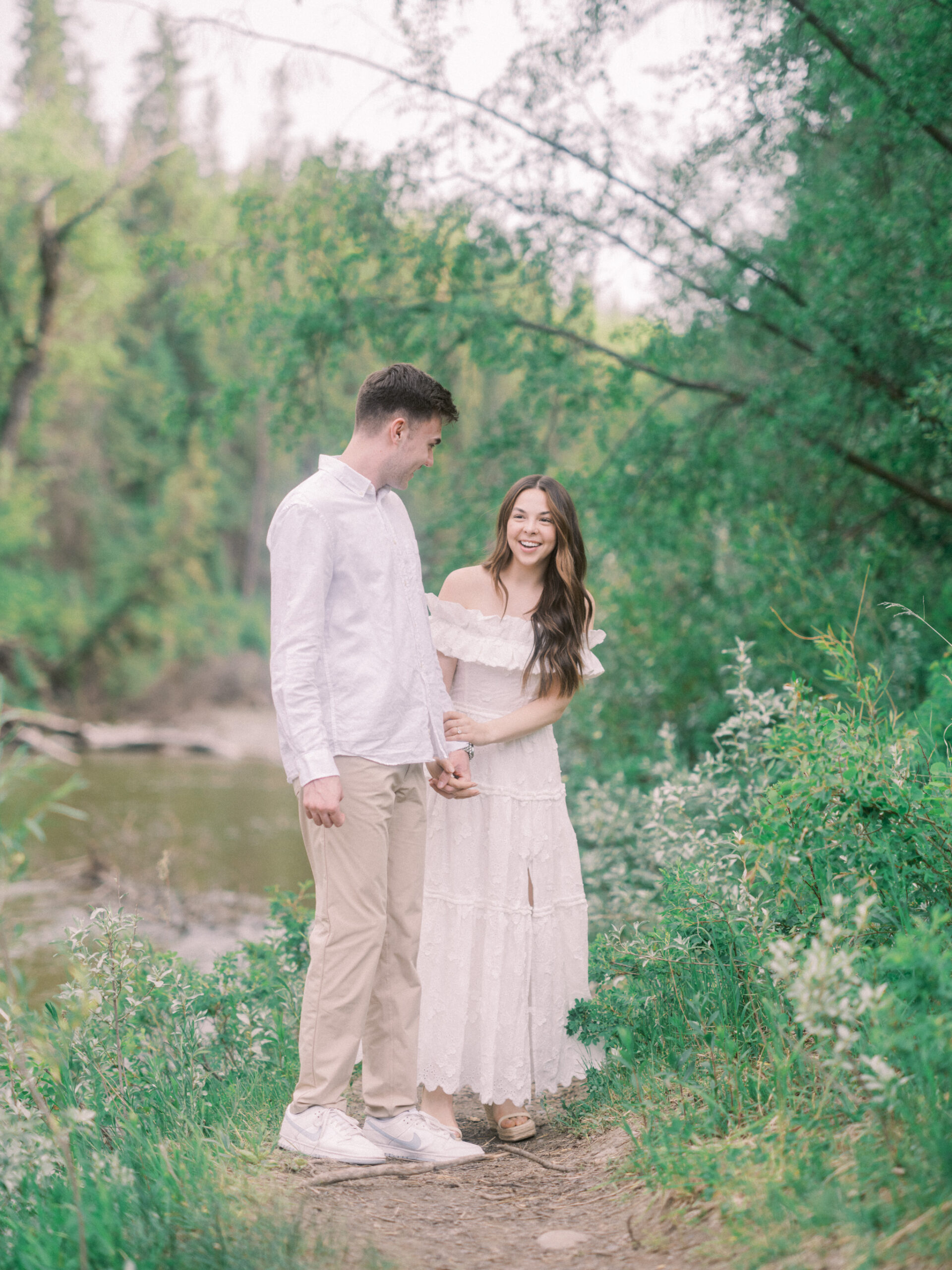 Riverside calgary engagement, forest engagement, bride in white ruffled dress engagement, groom and bride sitting by the river, bride and groom standing in river, standing in sunset forest, nicole sarah, calgary wedding photographers, fish creek park engagement