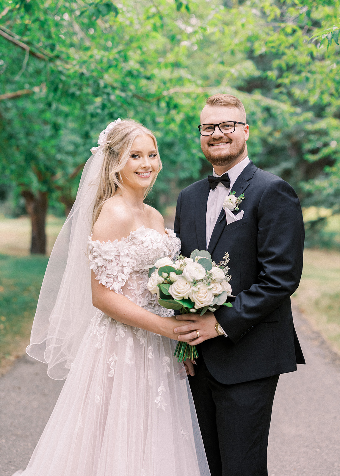 bride and groom embracing looking at the camera, calgary wedding couple, groom in black tuxedo, bride with lace drop sleeve gown, bride with long blonde curls, The Ultimate Calgary Wedding Photography Guide: Everything You Need to Know Before Your Wedding
